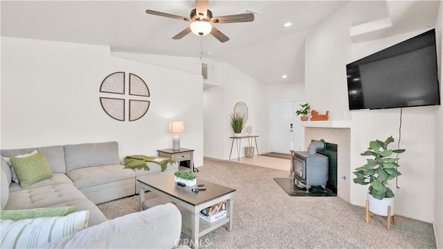 living room featuring ceiling fan, light colored carpet, vaulted ceiling, and a wood stove