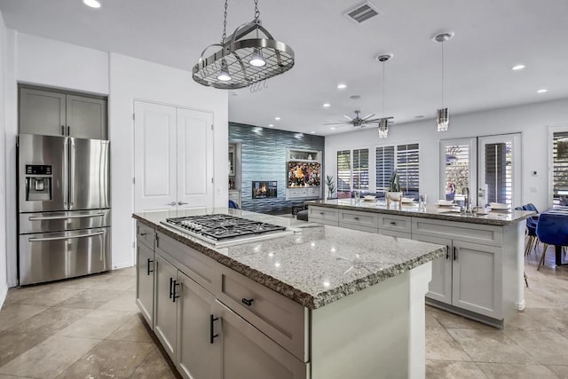 kitchen featuring light stone countertops, a high end fireplace, a kitchen island, decorative light fixtures, and stainless steel appliances