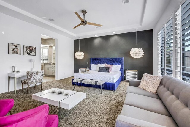 carpeted bedroom featuring ceiling fan, a tray ceiling, and ensuite bath