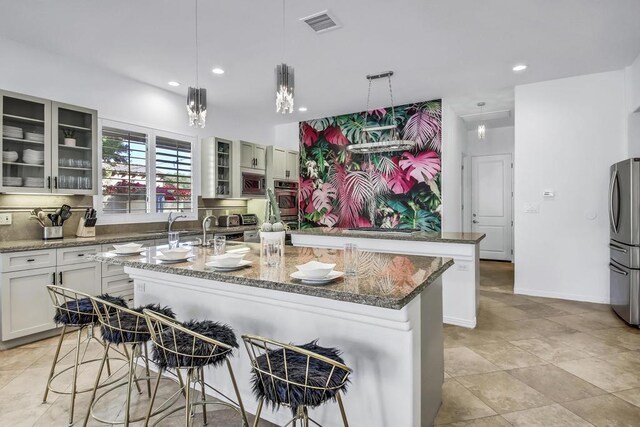 kitchen featuring light stone counters, hanging light fixtures, a center island with sink, and stainless steel appliances