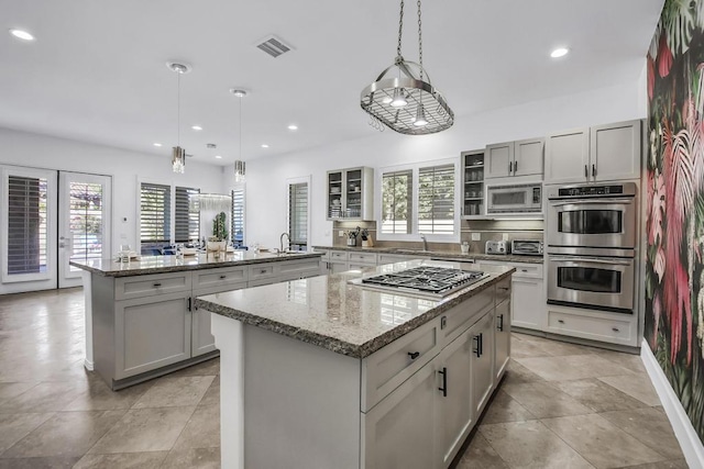 kitchen with light stone countertops, a kitchen island, stainless steel appliances, and decorative light fixtures