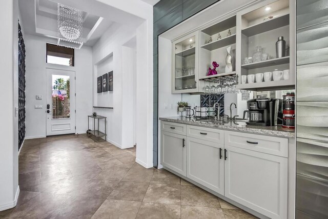 bar with white cabinets, a notable chandelier, sink, and light stone counters