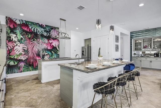 kitchen featuring dark stone countertops, sink, hanging light fixtures, stainless steel fridge with ice dispenser, and a kitchen island with sink