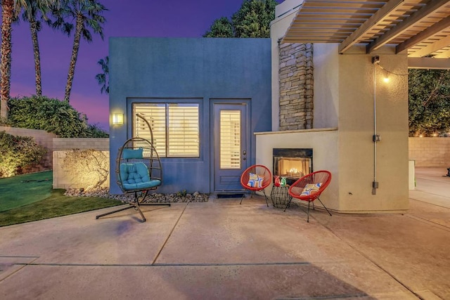 back house at dusk featuring exterior fireplace and a patio area