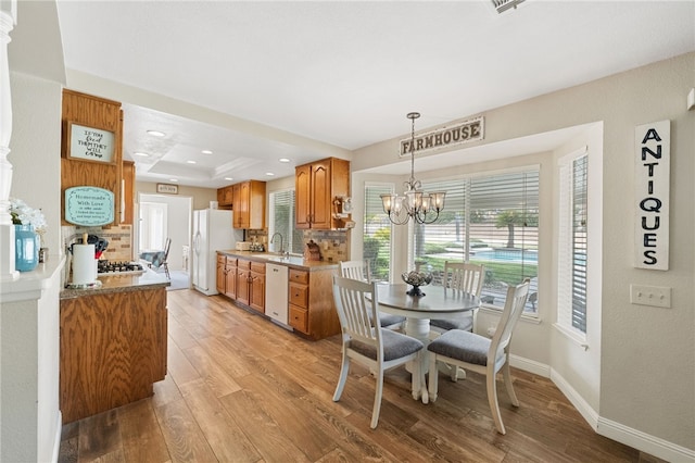 dining room with sink, light hardwood / wood-style flooring, a raised ceiling, and a notable chandelier