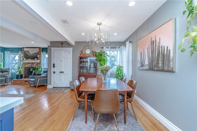 dining room with beam ceiling, a fireplace, an inviting chandelier, and light hardwood / wood-style floors