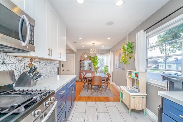 kitchen with blue cabinetry, stainless steel appliances, white cabinets, and an inviting chandelier