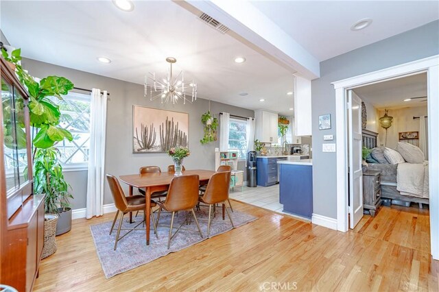 dining area with light wood-type flooring, plenty of natural light, and an inviting chandelier