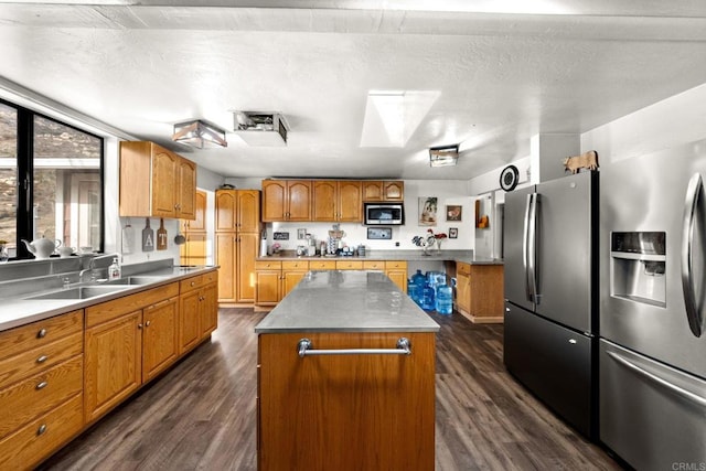 kitchen with a skylight, appliances with stainless steel finishes, dark hardwood / wood-style floors, a kitchen island, and sink