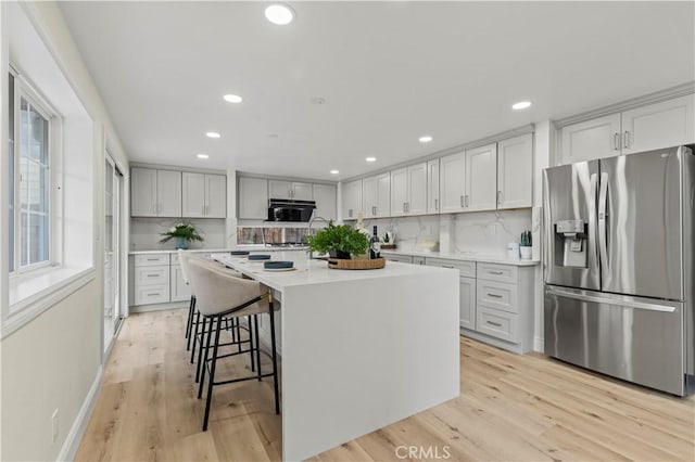 kitchen featuring light hardwood / wood-style flooring, a kitchen island with sink, stainless steel fridge with ice dispenser, and a kitchen bar