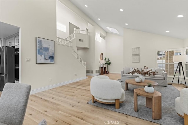 living room featuring a skylight, a towering ceiling, and light hardwood / wood-style flooring