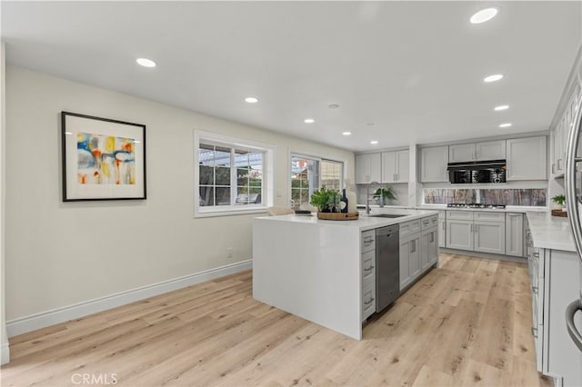 kitchen featuring a center island with sink, stainless steel appliances, tasteful backsplash, light hardwood / wood-style flooring, and sink