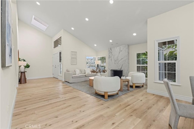 living room with high vaulted ceiling, light hardwood / wood-style flooring, a skylight, and a premium fireplace