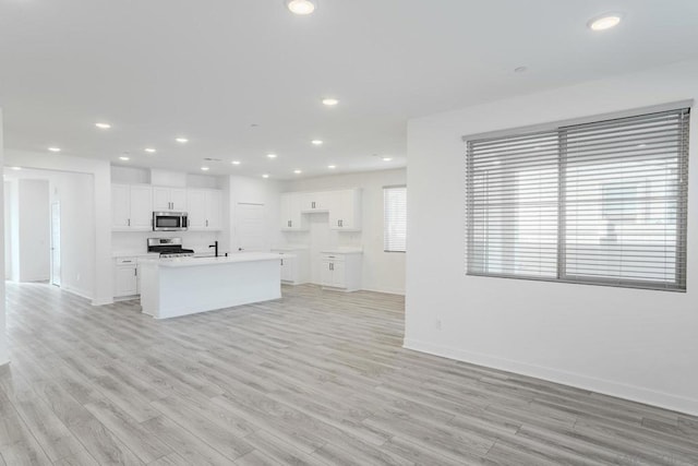 kitchen featuring sink, white cabinetry, light wood-type flooring, appliances with stainless steel finishes, and an island with sink