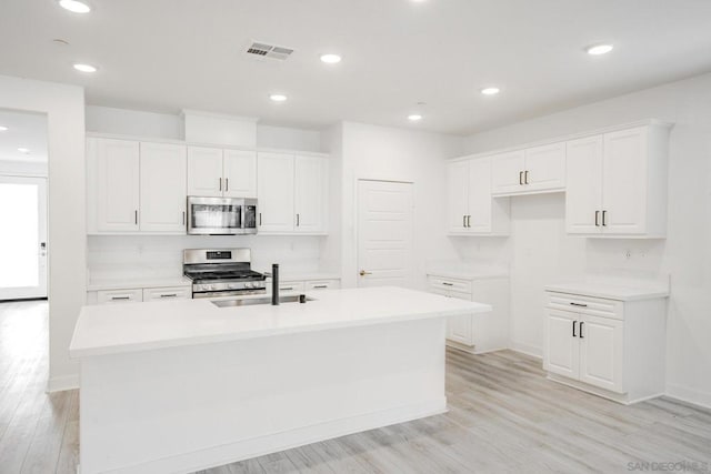 kitchen featuring stainless steel appliances, a kitchen island with sink, light wood-type flooring, white cabinets, and sink