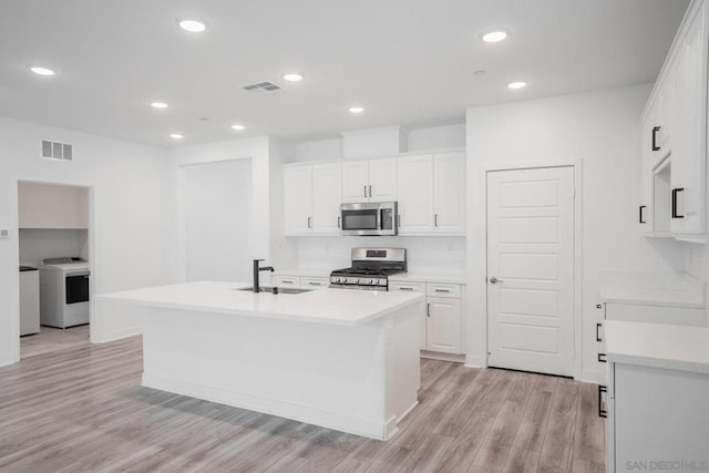 kitchen with washer / dryer, white cabinetry, stainless steel appliances, an island with sink, and sink