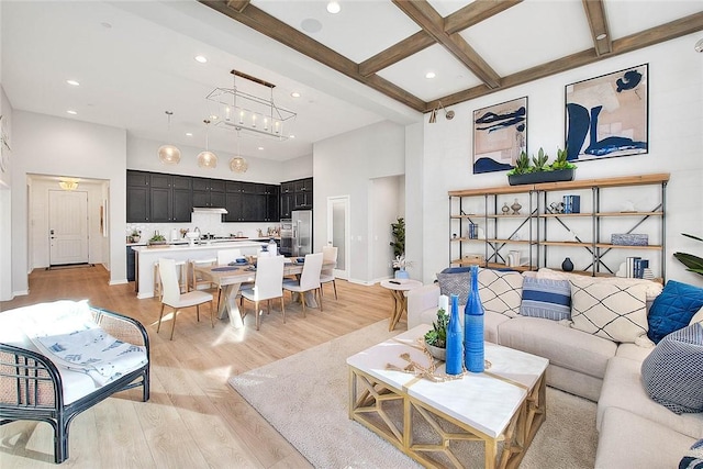 living room with a notable chandelier, beamed ceiling, coffered ceiling, a high ceiling, and light hardwood / wood-style flooring