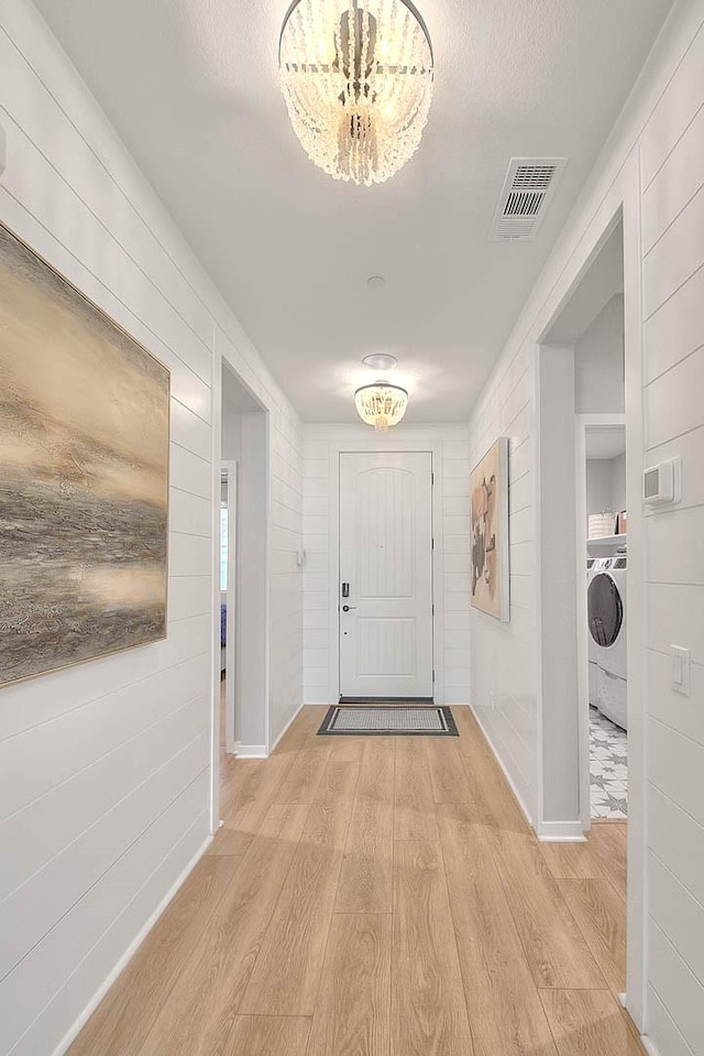 entrance foyer with washer / clothes dryer, light hardwood / wood-style floors, and an inviting chandelier