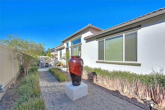 view of property exterior with a patio area, a fenced backyard, a tile roof, and stucco siding