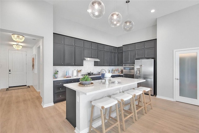 kitchen with a kitchen bar, decorative light fixtures, a high ceiling, an island with sink, and stainless steel appliances