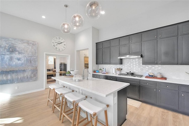 kitchen with light hardwood / wood-style flooring, a kitchen bar, an island with sink, hanging light fixtures, and stainless steel gas stovetop