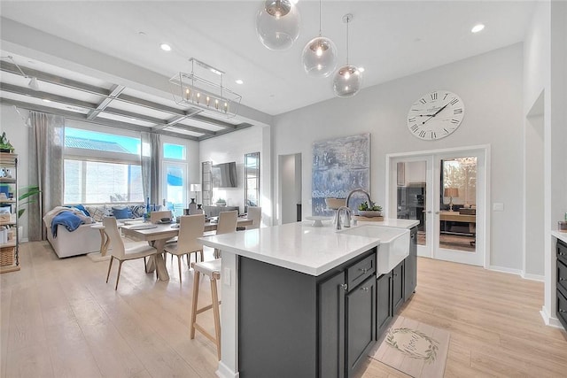 kitchen featuring pendant lighting, sink, an island with sink, coffered ceiling, and beamed ceiling