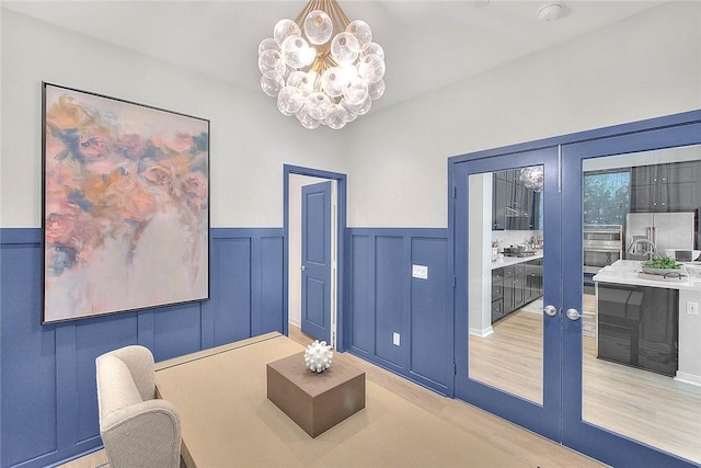 interior space with light wood finished floors, wainscoting, and an inviting chandelier