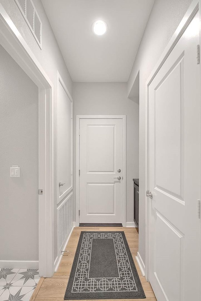 corridor with light wood finished floors, baseboards, and visible vents