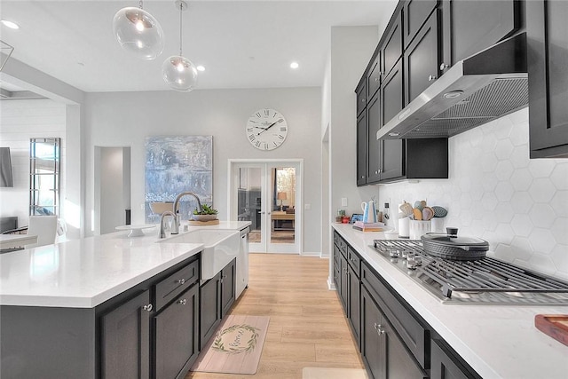 kitchen featuring stainless steel gas stovetop, tasteful backsplash, hanging light fixtures, sink, and an island with sink