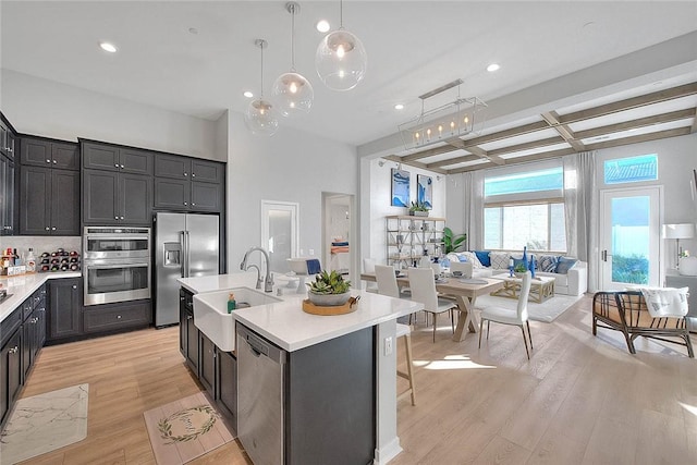 kitchen with pendant lighting, appliances with stainless steel finishes, an island with sink, beam ceiling, and coffered ceiling