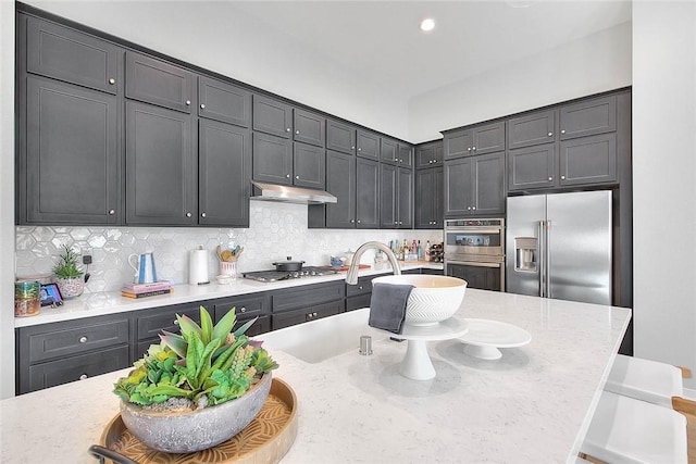 kitchen with a kitchen breakfast bar, backsplash, light stone counters, a kitchen island with sink, and stainless steel appliances