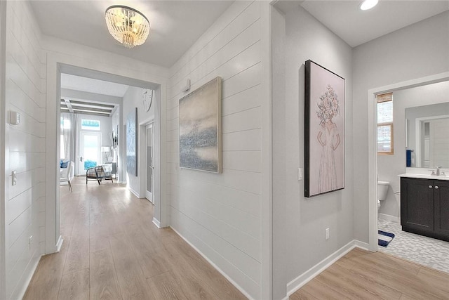 hallway featuring sink, a chandelier, and light wood-type flooring