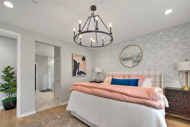 bedroom with light wood-type flooring, ensuite bath, and a notable chandelier