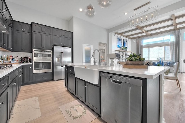 kitchen featuring stainless steel appliances, sink, hanging light fixtures, a center island with sink, and beam ceiling