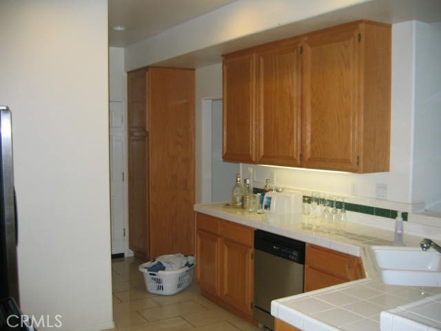 kitchen featuring sink, dishwasher, tile counters, and light tile patterned flooring