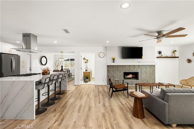 living room featuring light wood-type flooring, ceiling fan, and a tiled fireplace