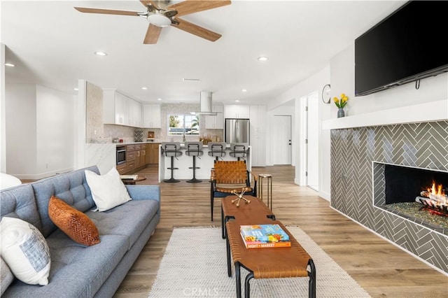 living room featuring ceiling fan, a tile fireplace, and light wood-type flooring