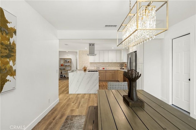 kitchen featuring ventilation hood, light hardwood / wood-style flooring, tasteful backsplash, and an inviting chandelier