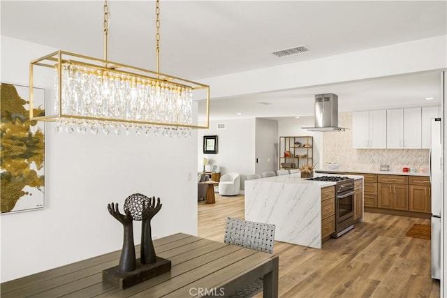 kitchen with tasteful backsplash, high end range, light hardwood / wood-style floors, white cabinetry, and wall chimney exhaust hood