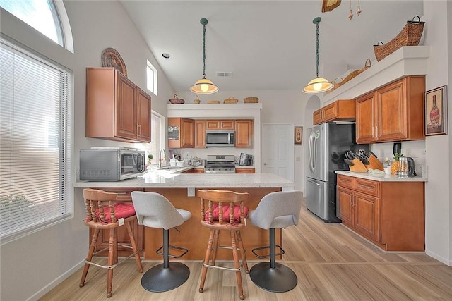 kitchen featuring light wood-type flooring, hanging light fixtures, kitchen peninsula, and appliances with stainless steel finishes