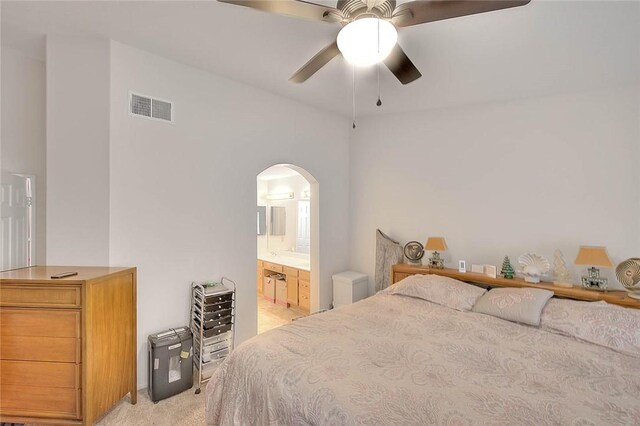 bedroom with ceiling fan, light carpet, and ensuite bath