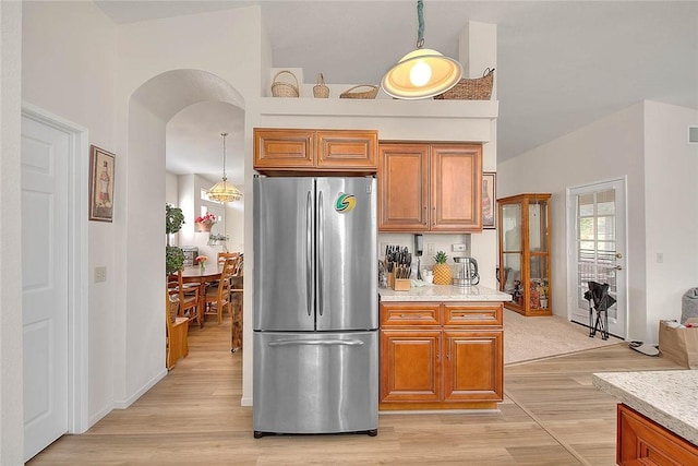 kitchen with decorative light fixtures, light hardwood / wood-style flooring, light stone countertops, and stainless steel fridge