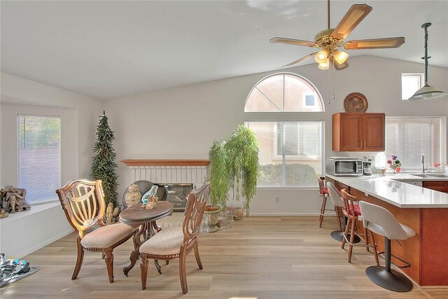 kitchen featuring lofted ceiling, decorative light fixtures, ceiling fan, a brick fireplace, and light hardwood / wood-style flooring