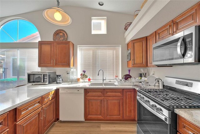 kitchen with sink, decorative light fixtures, stainless steel appliances, light stone counters, and lofted ceiling