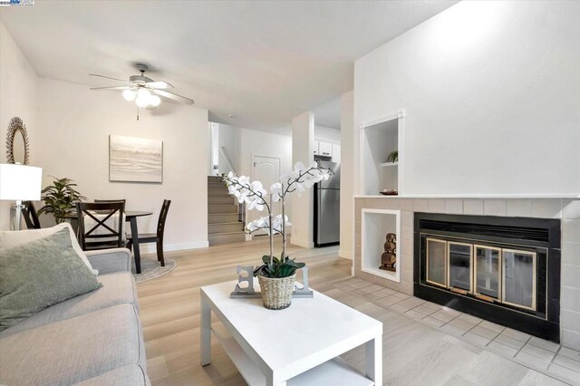 living room with ceiling fan, light hardwood / wood-style floors, built in features, and a fireplace