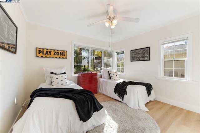 bedroom featuring ceiling fan, light wood-type flooring, crown molding, and multiple windows