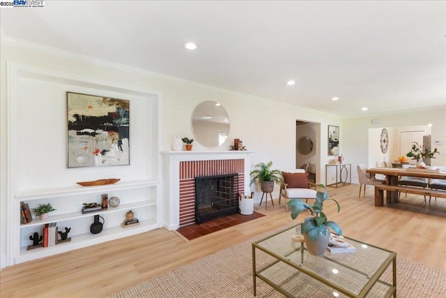 living room with built in features, a fireplace, ornamental molding, and hardwood / wood-style floors