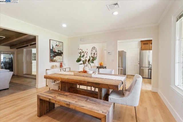 dining area featuring ornamental molding, light hardwood / wood-style floors, and vaulted ceiling with beams