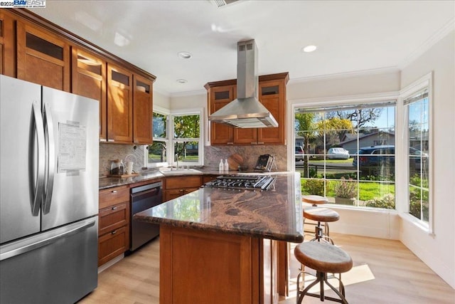 kitchen with appliances with stainless steel finishes, a center island, wall chimney exhaust hood, a kitchen bar, and dark stone counters