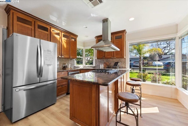 kitchen featuring dark stone countertops, a center island, light wood-type flooring, appliances with stainless steel finishes, and island range hood